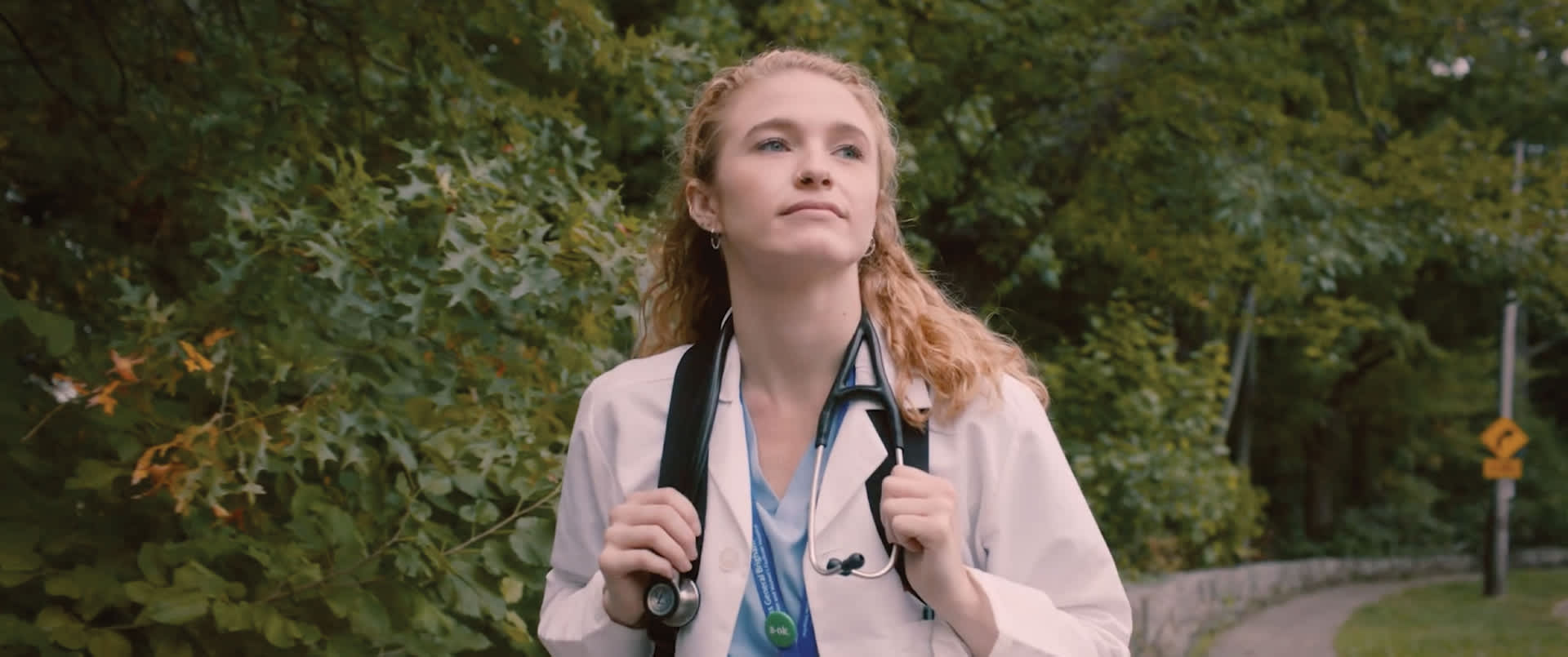 A healthcare professional stands amidst a backdrop of greenery