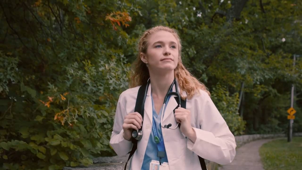 A healthcare professional stands amidst a backdrop of greenery