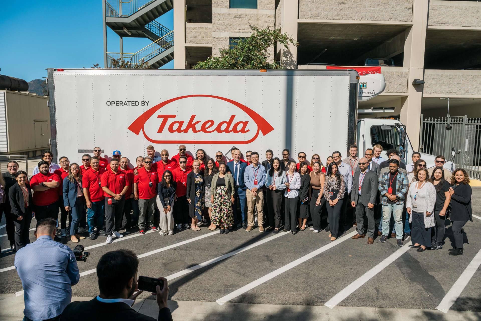 Large group standing in front of a Takeda-branded truck in a parking lot.