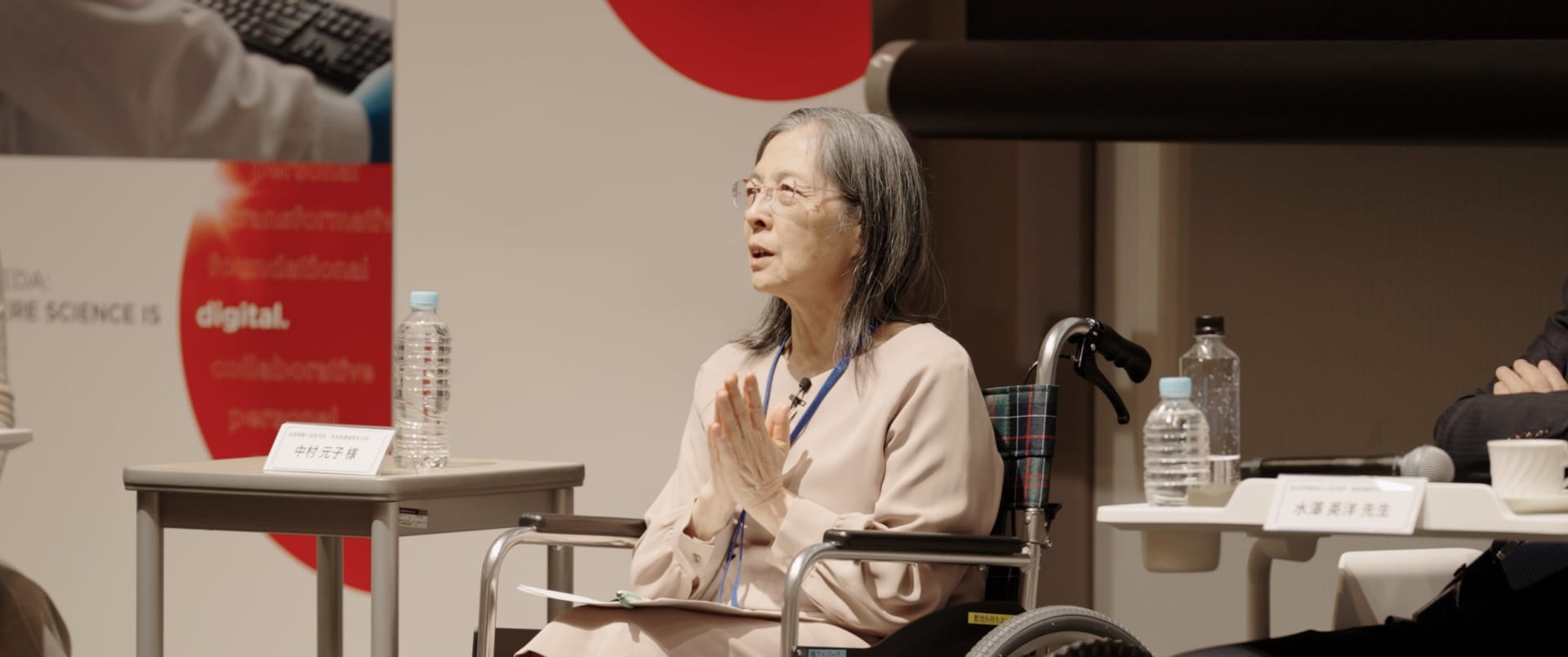 A person in a wheelchair is participating in a panel discussion at an event.