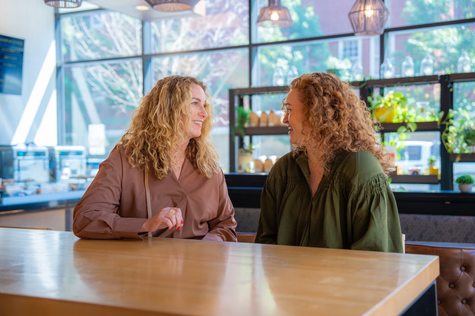 Photograph of two women sitting at a wooden table in a bright cafe