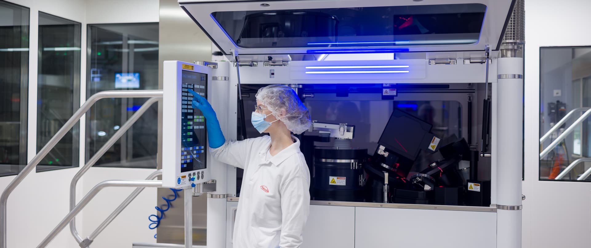 Person in protective clothing operates a touchscreen panel on an automated machine in a cleanroom.