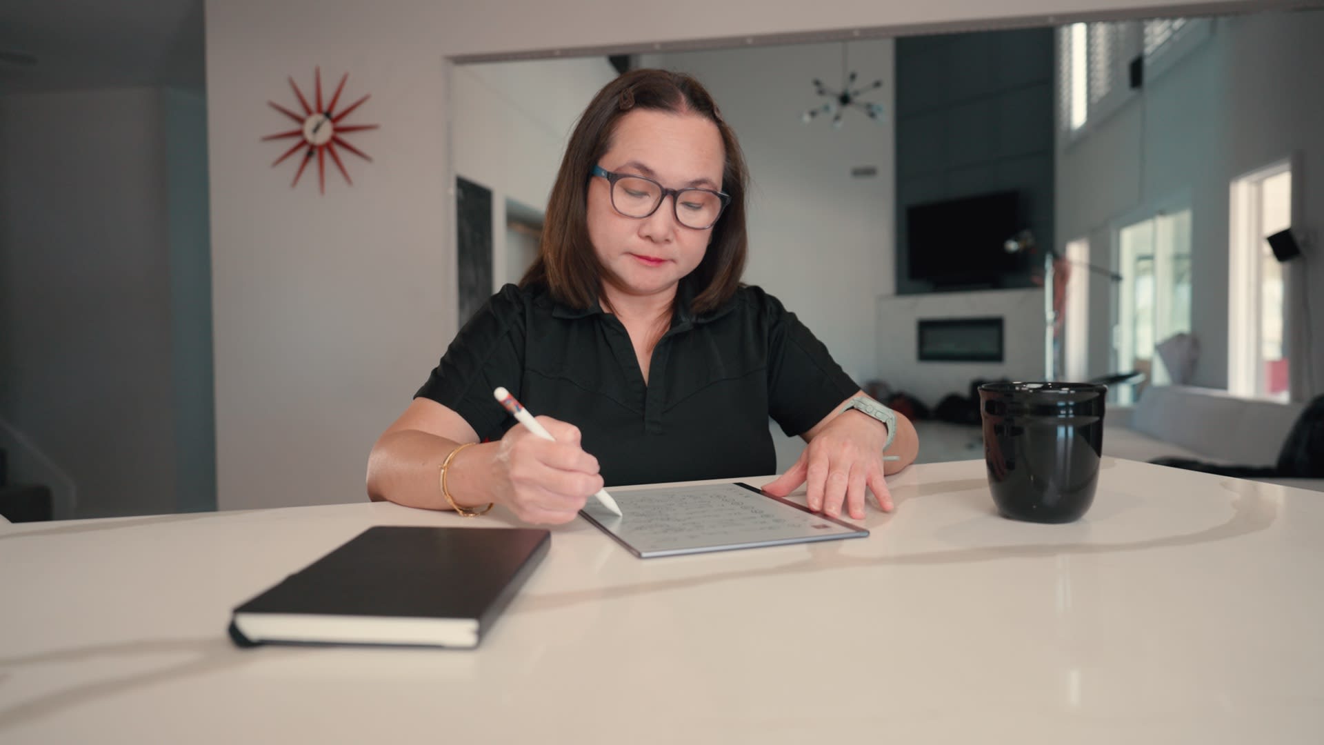 Photograph shows a woman writing in a notebook at a white desk