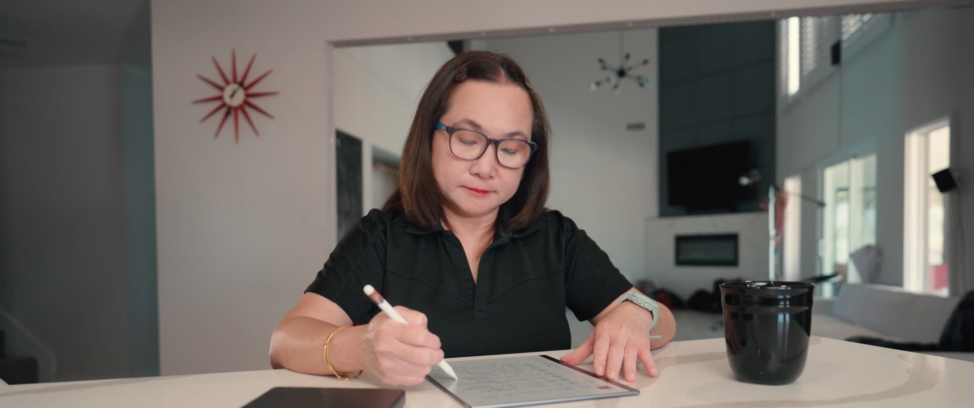 Photograph shows a woman writing in a notebook at a white desk