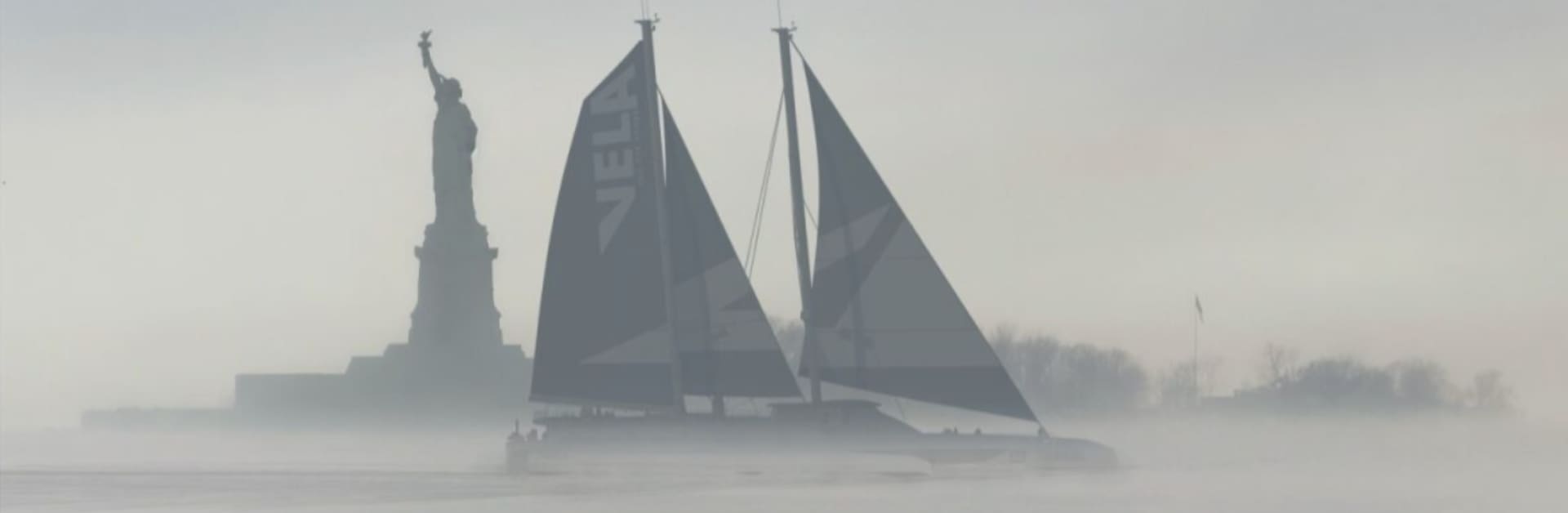Sailboat with dark sails in misty waters near the Statue of Liberty.