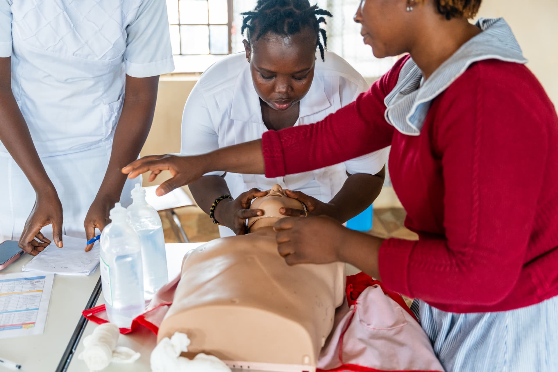 Nurses practice pediatric emergency care using a training mannequin and medical supplies.