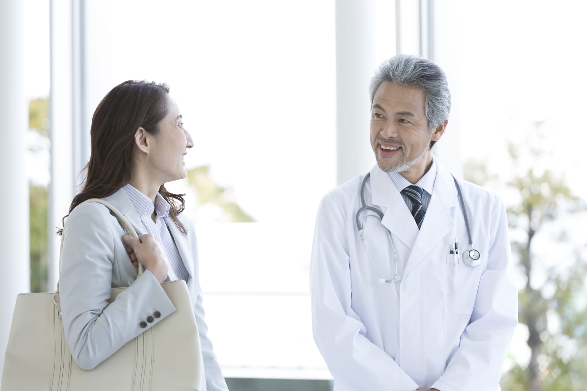 白衣を着た医療従事者とビジネスバッグを持つ人物が屋内で会話している様子