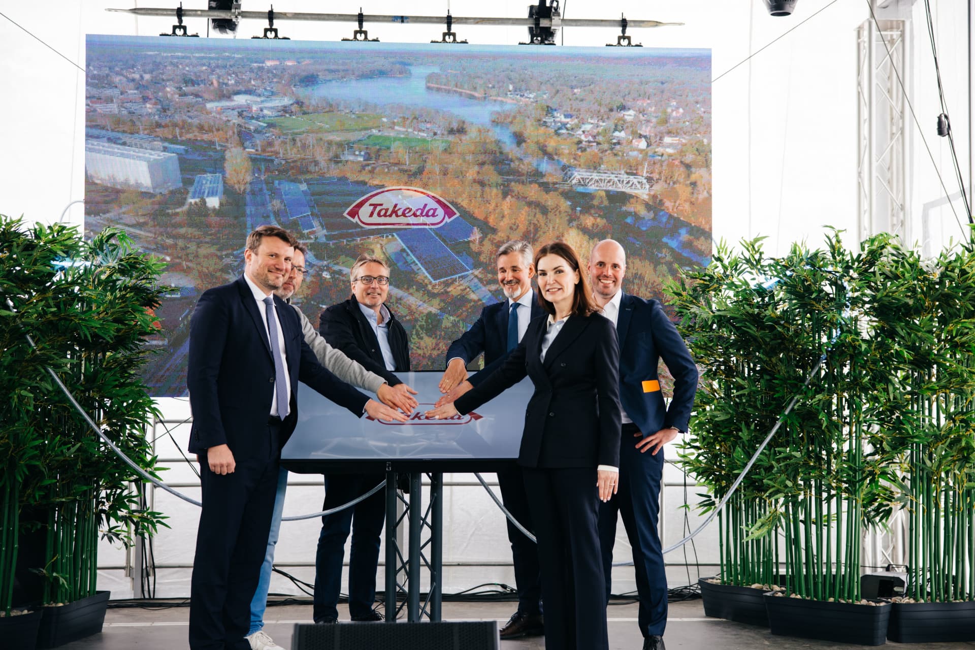 Photograph showing five business professionals standing around a table with hands joined over a Takeda logo