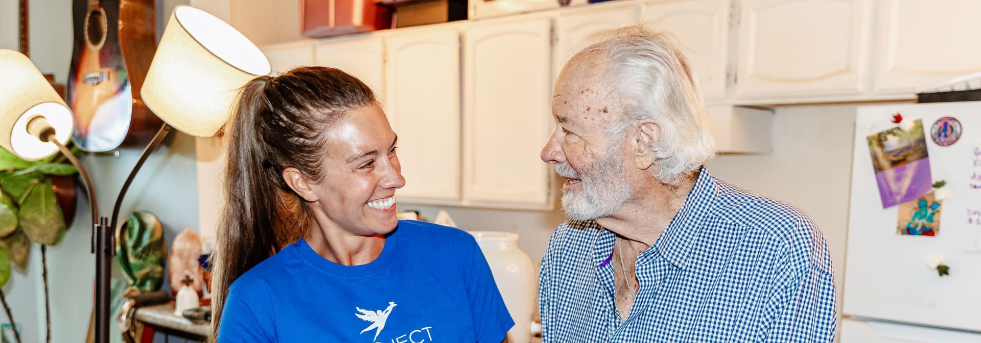 Photograph of three people wearing red shirts and pink aprons working in a kitchen
