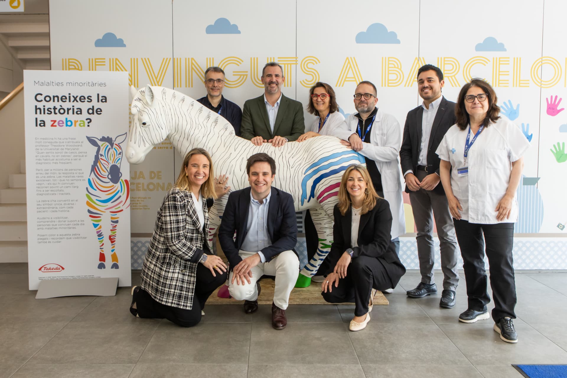 Photograph of a group of nine people posing around a life-sized zebra sculpture painted with colorful stripes inside a building