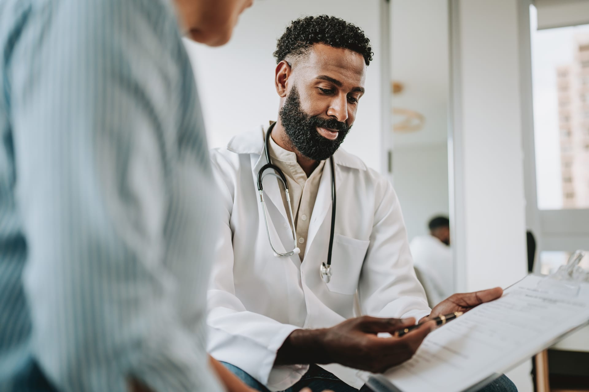 Photograph showing a doctor wearing a white coat and stethoscope reviewing a medical chart with a patient