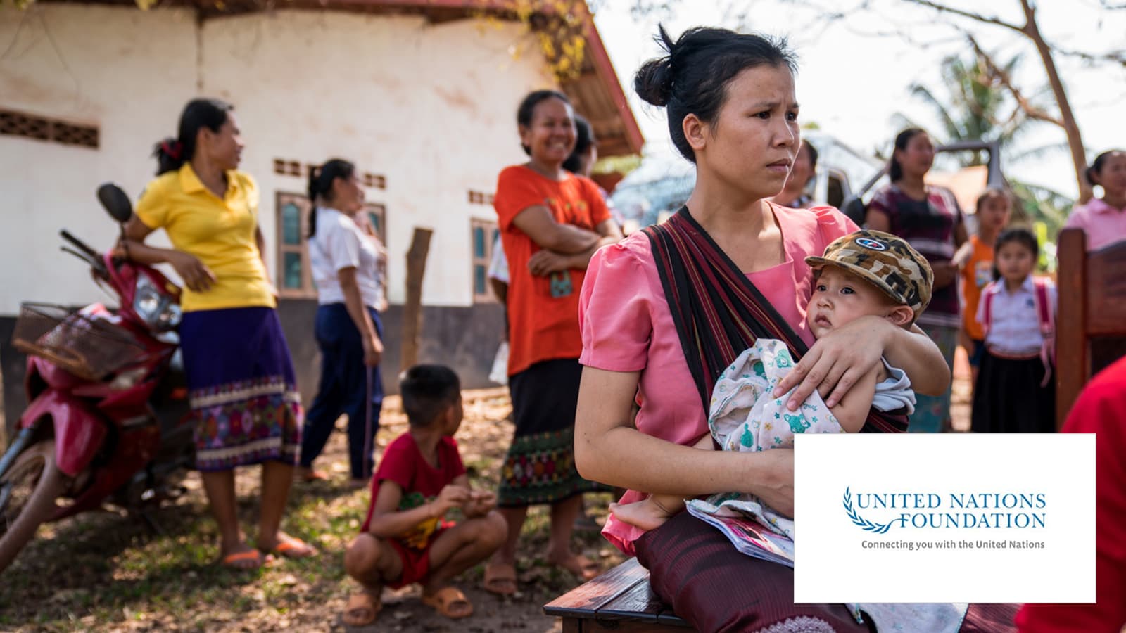 A woman carrying a child, in the back various people standing there