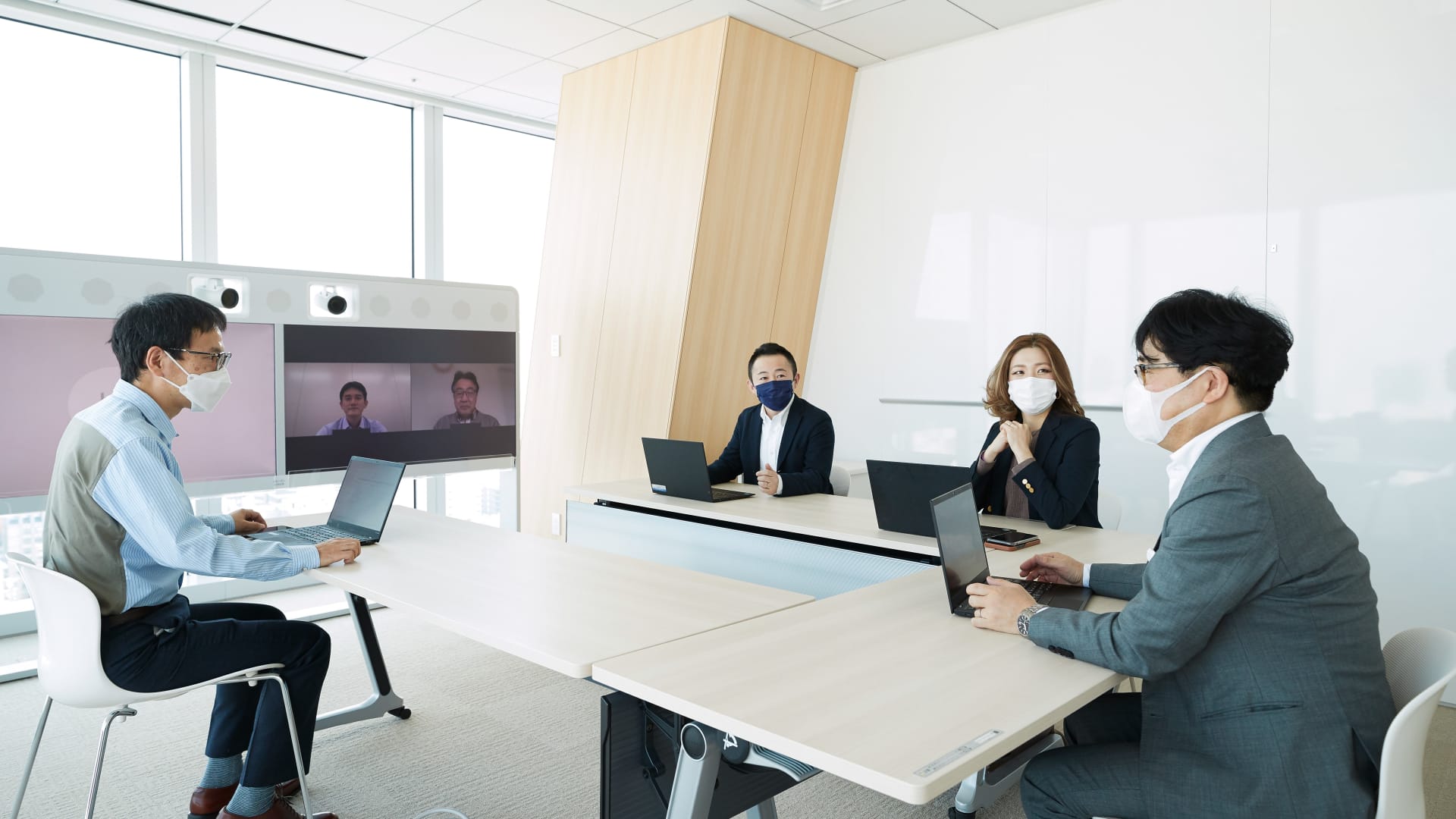 Four employees in a boardroom having a videocall with two more colleagues