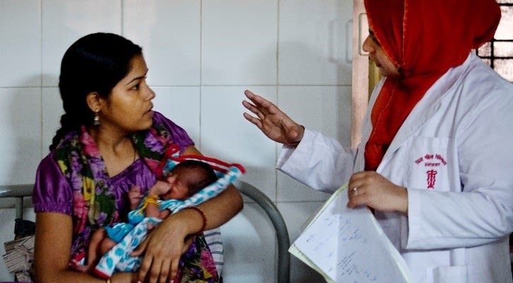 Mother carrying newborn while speaking to physician