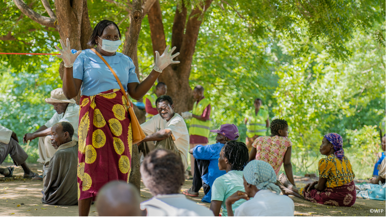 a women with gloves and face mask is talking to a group of people