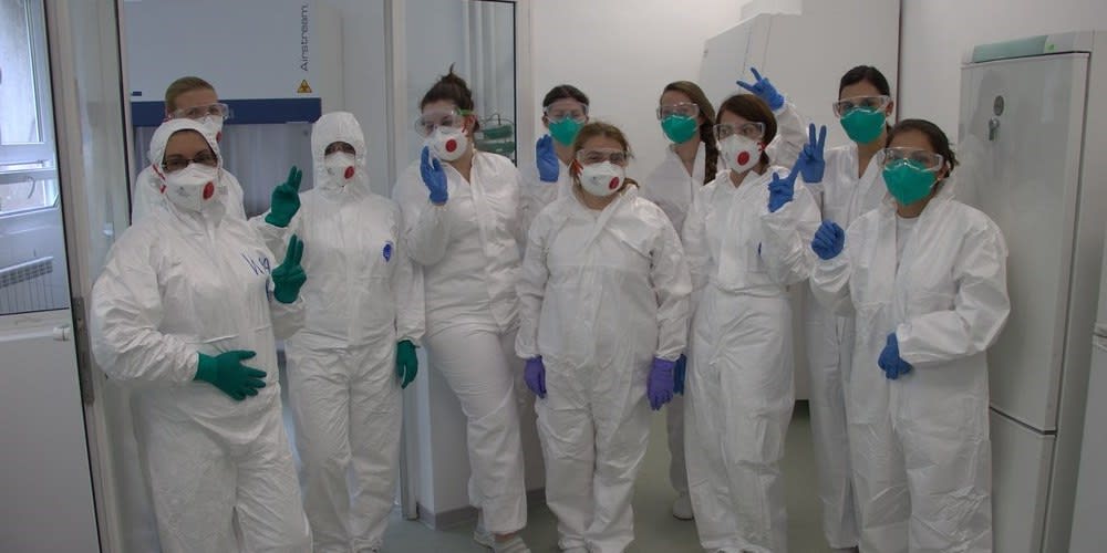 ten women standing in a lab wearing lab overalls