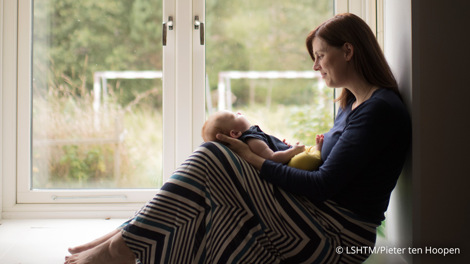 a mother is sitting on a window sill carrying her baby